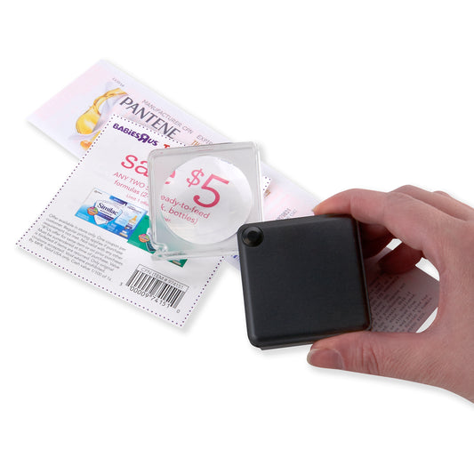Hand holding a small black flip-open magnifying glass over a coupon on a white background