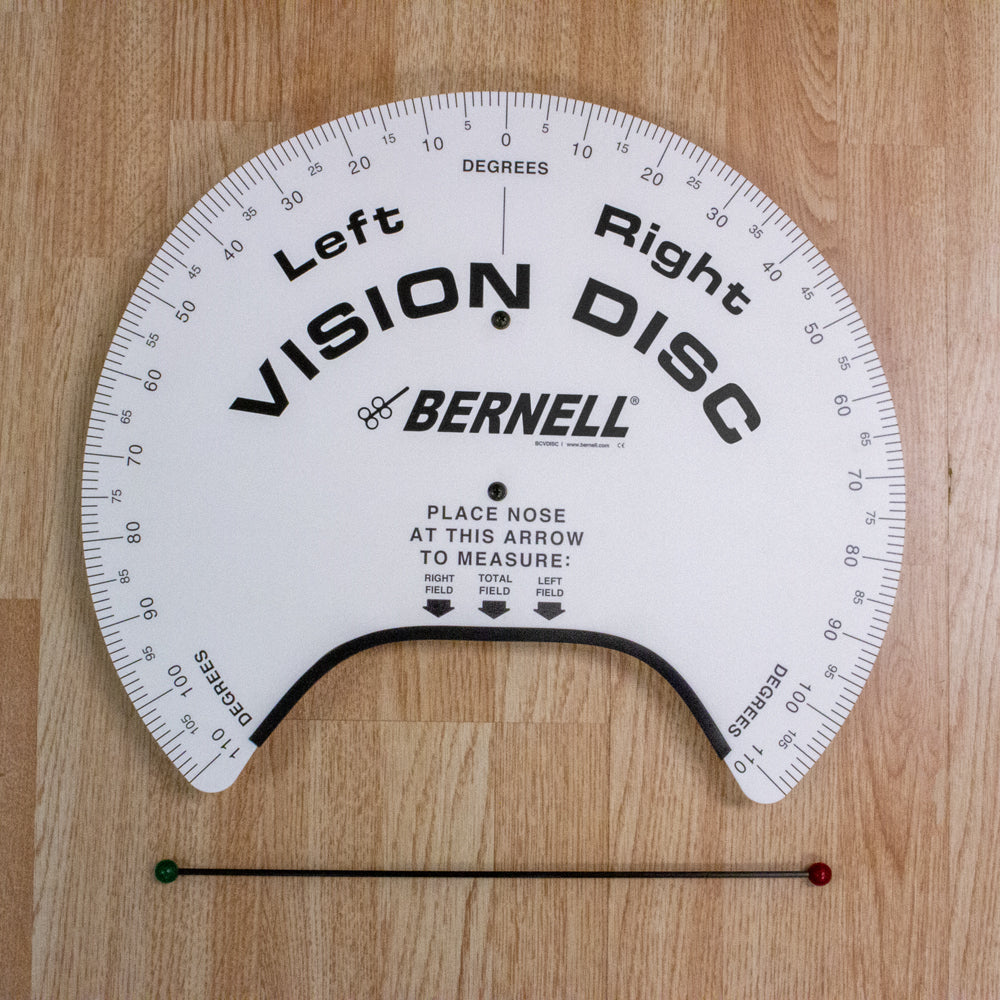 A BERNELL Vision Disc eye alignment test device with a white semi-circular dial, black printed text and markings, and a fixation wand with red and green ends, shown on a light wood background.