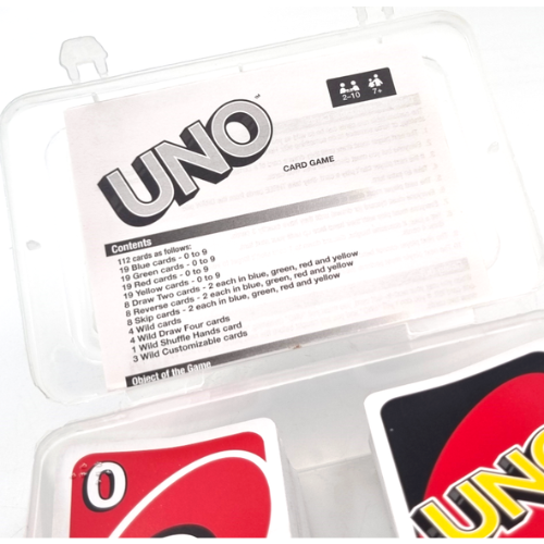 UNO card game box and cards in a clear plastic clamshell case, showing the front cover, contents list, and partial card designs showing Braille print in the top left corner of the cards.