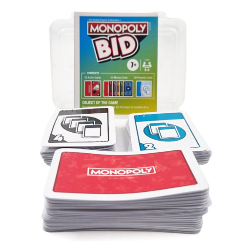 Monopoly Bid card game set with a clear plastic storage container, showing the front of the box and several stacks of cards in front on a white background.